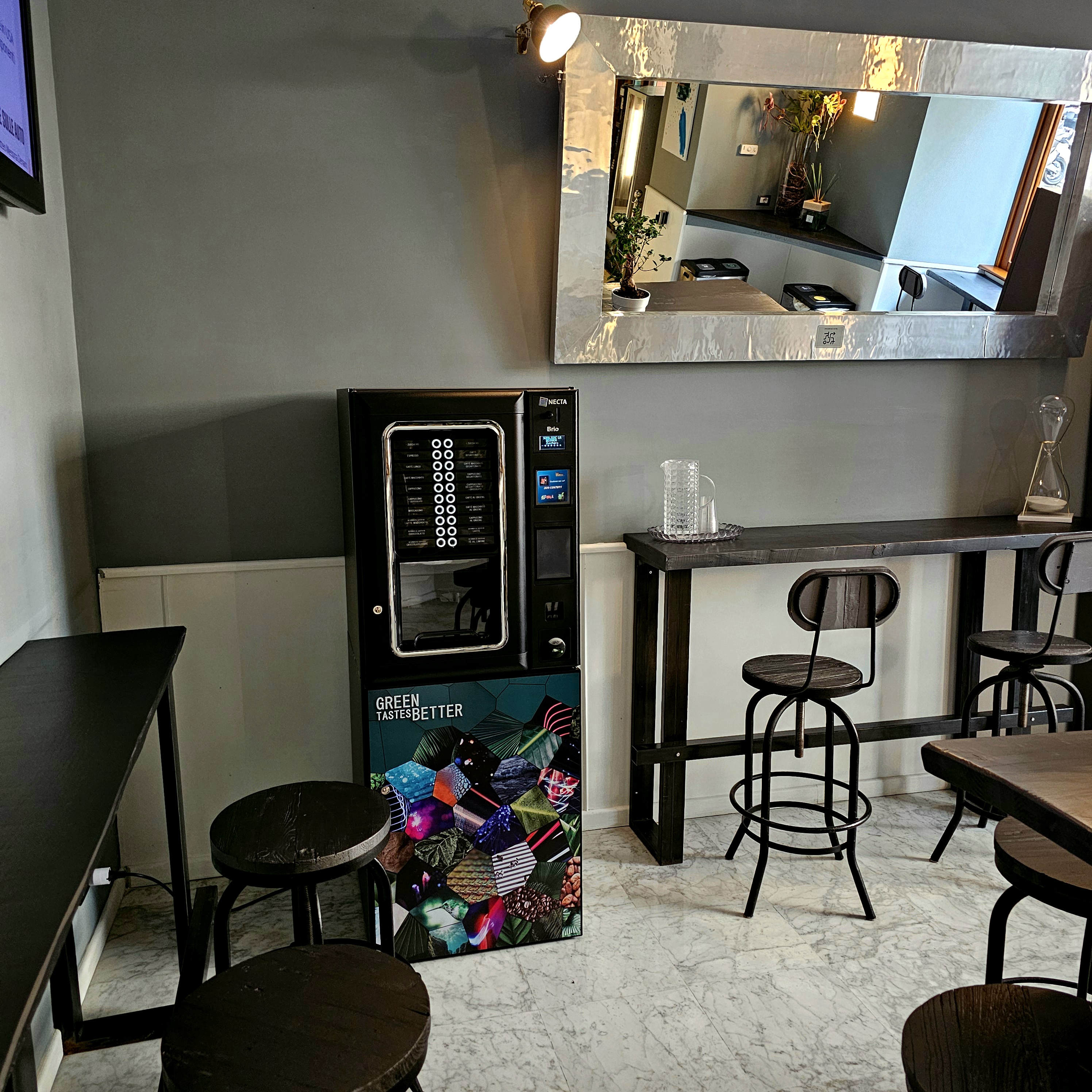 Distributore di caffè inserito in uno spazio con tavolini e sedute